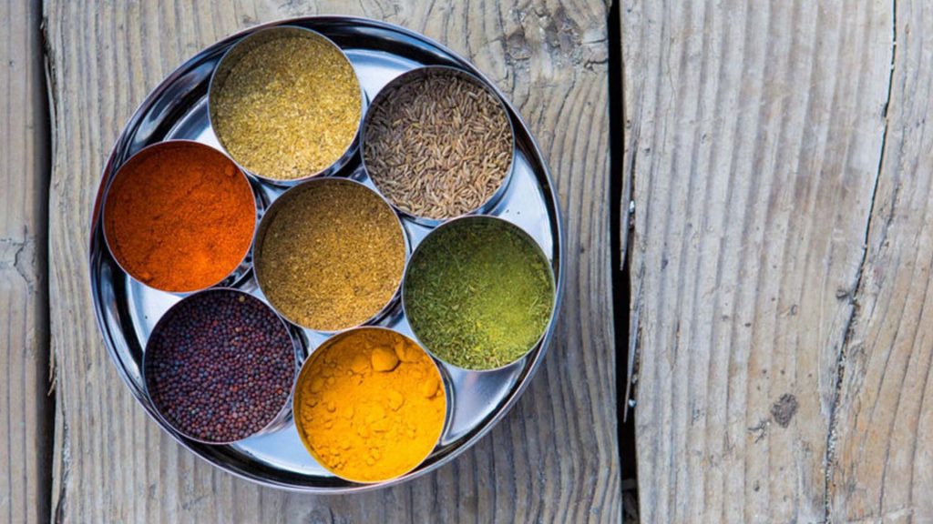 a tray of 7 brightly colored spices on a wood grain background
