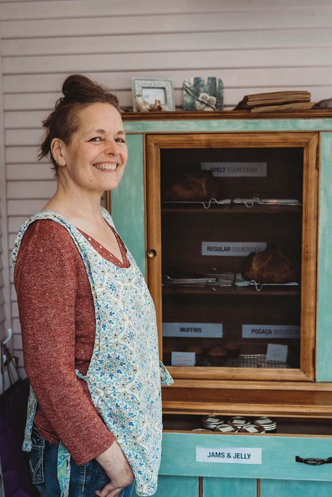 Marianne stands in front of a cabinet with bread and pastries inside the Farm Stand