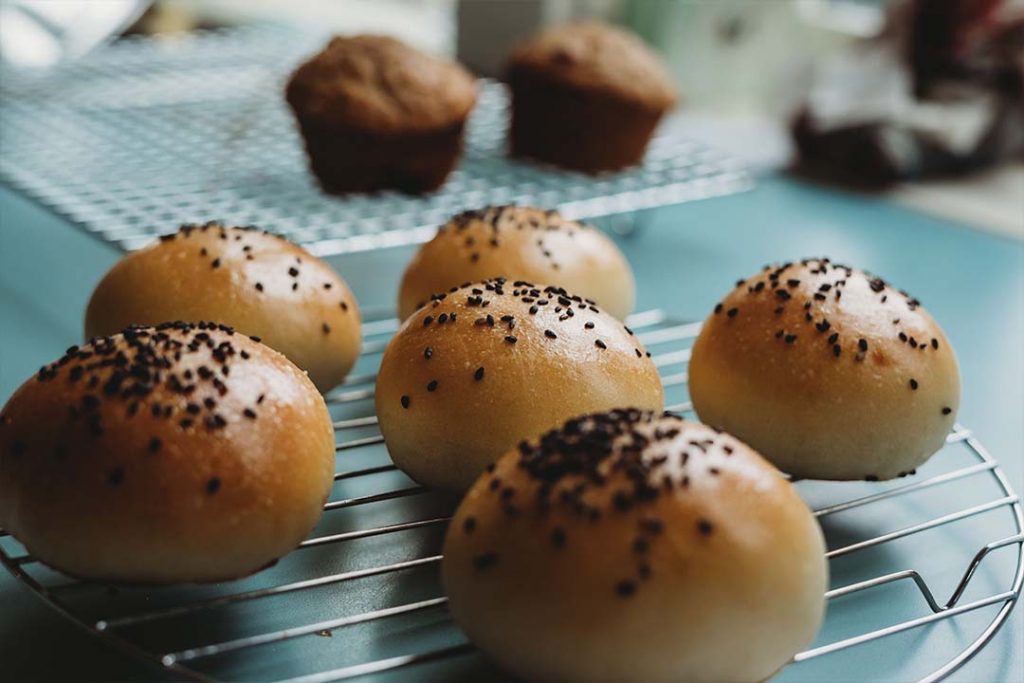 Round pastries with black sesame seeds sprinkled on top rest on a cooling rack.