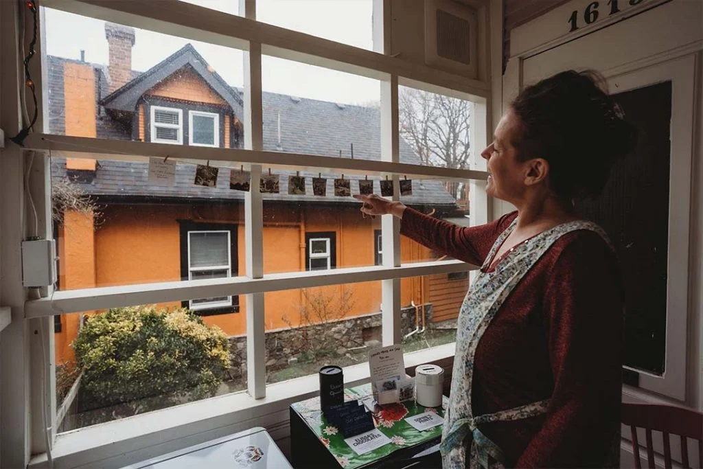 Marianne points to little paintings that hang on a string in a window of the Farm Stand