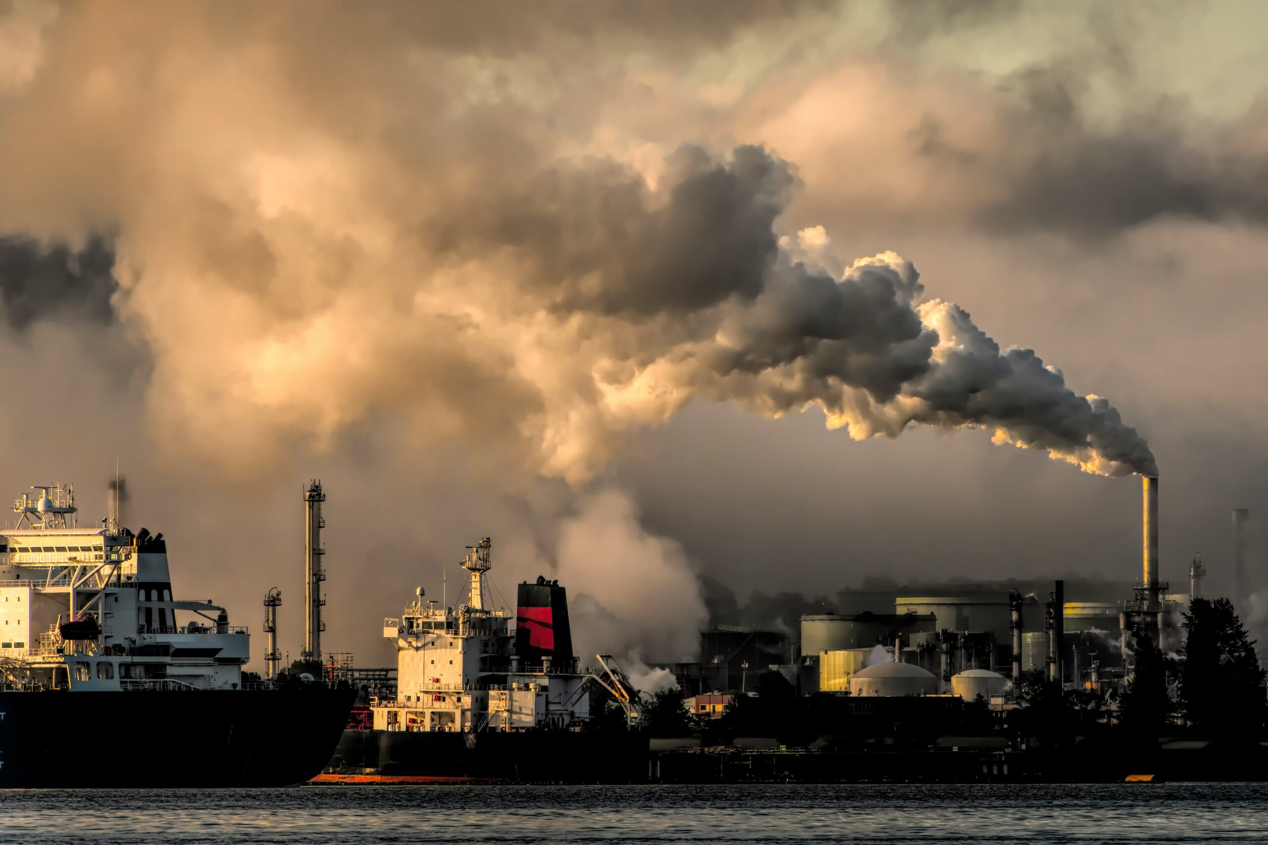 Image of coastal oil refinery with smoke coming out of a chimney, meant to illustrate pollution caused from fossil fuel industry.